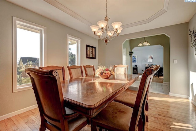 dining area featuring light wood-type flooring, a wealth of natural light, a raised ceiling, and an inviting chandelier