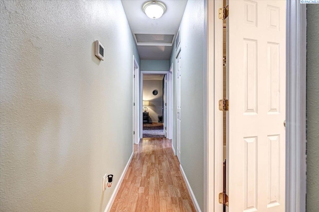 hallway featuring baseboards, a textured wall, and light wood finished floors