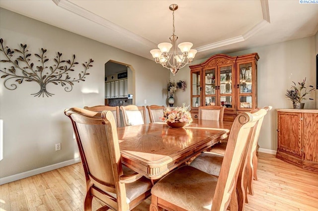 dining space featuring light wood-style floors, a tray ceiling, a notable chandelier, and baseboards