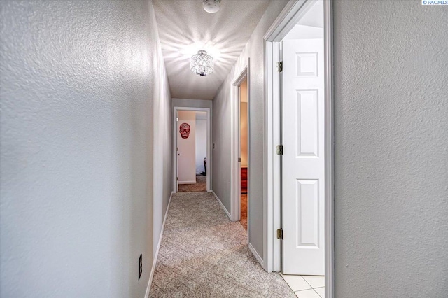 hallway featuring light carpet, a textured wall, and baseboards