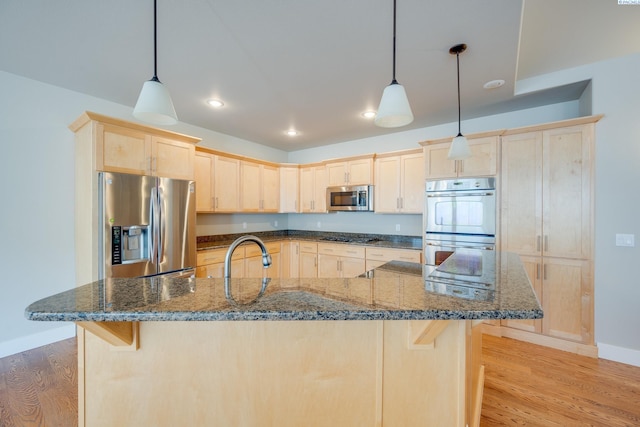 kitchen featuring decorative light fixtures, light hardwood / wood-style floors, dark stone counters, and appliances with stainless steel finishes