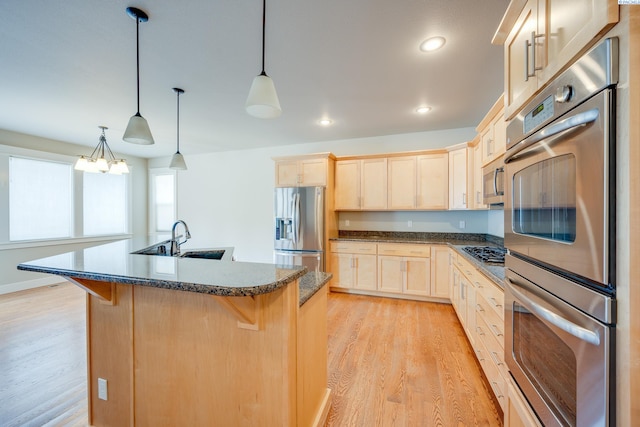 kitchen featuring a kitchen island with sink, sink, decorative light fixtures, and stainless steel appliances