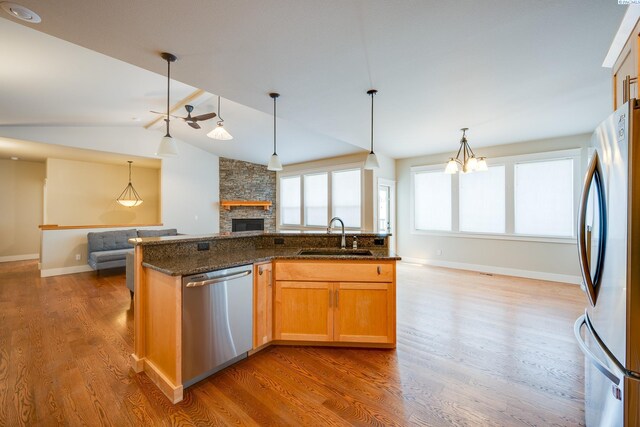 kitchen featuring a stone fireplace, sink, dark stone countertops, appliances with stainless steel finishes, and dark hardwood / wood-style flooring