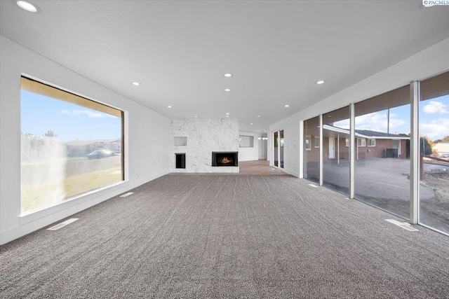 unfurnished living room with carpet floors, a wealth of natural light, and a large fireplace