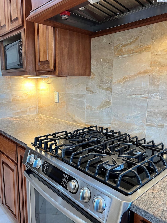 details featuring dark stone countertops, gas range, decorative backsplash, and premium range hood