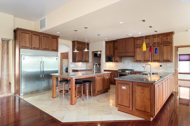 kitchen with sink, decorative light fixtures, built in appliances, dark stone countertops, and a kitchen breakfast bar