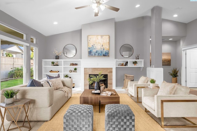 living room with ceiling fan, a tiled fireplace, and vaulted ceiling