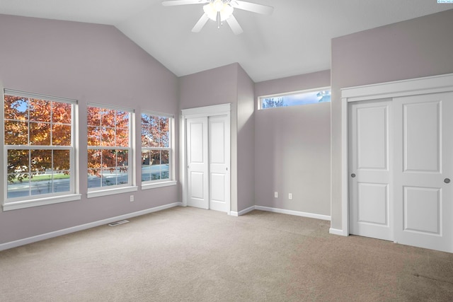 unfurnished bedroom featuring multiple closets, vaulted ceiling, light colored carpet, and ceiling fan