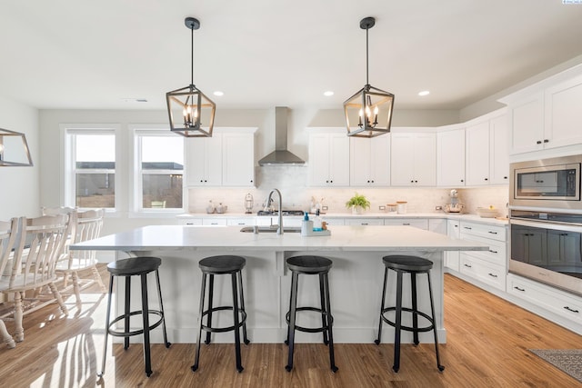 kitchen featuring white cabinets, stainless steel appliances, light wood-type flooring, wall chimney range hood, and backsplash