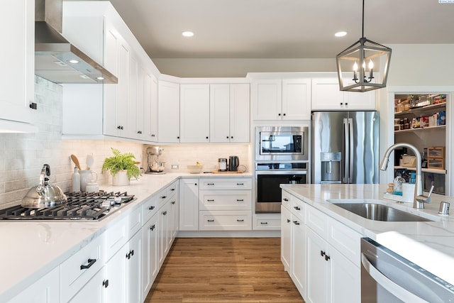 kitchen featuring light wood finished floors, wall chimney exhaust hood, appliances with stainless steel finishes, white cabinetry, and a sink