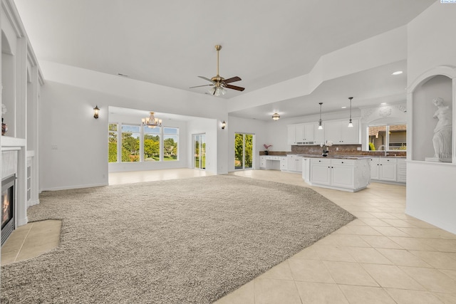 living room featuring ceiling fan with notable chandelier, a tiled fireplace, light tile patterned flooring, and baseboards