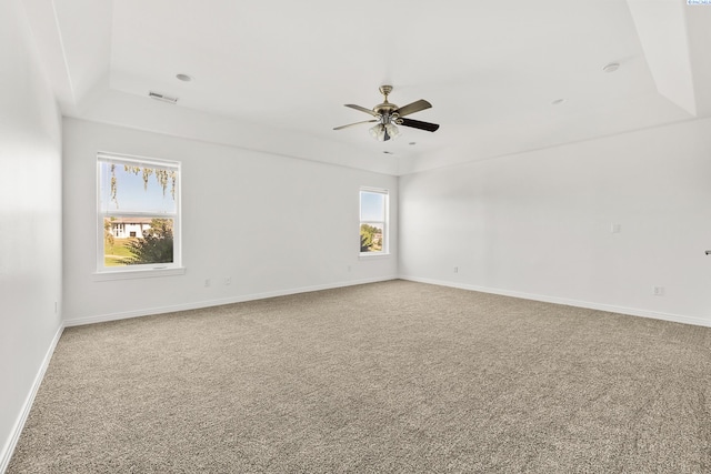 carpeted spare room featuring a tray ceiling, a ceiling fan, visible vents, and baseboards