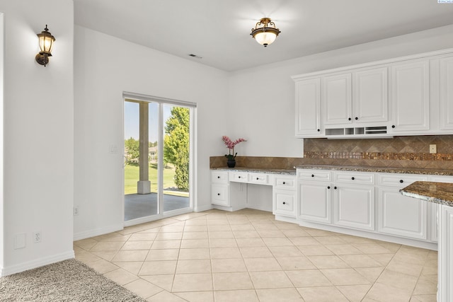 kitchen featuring dark stone counters, built in study area, white cabinetry, and decorative backsplash