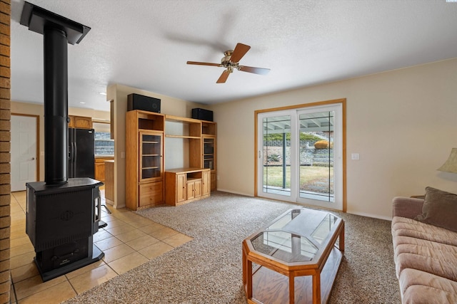 living area featuring ceiling fan, a textured ceiling, light carpet, and a wood stove