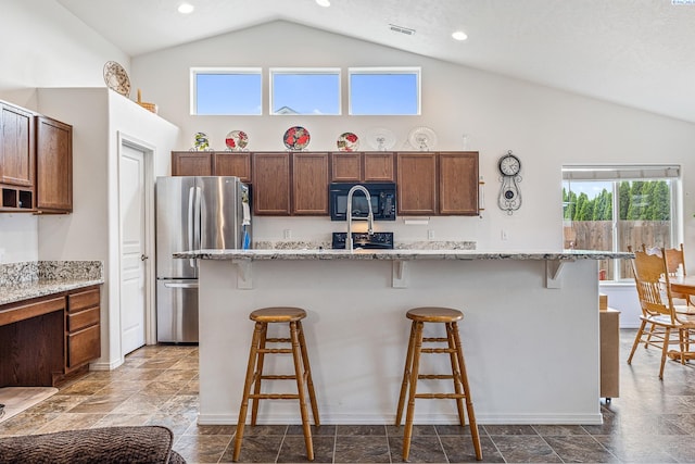 6110 Westport Ln, Pasco, WA 99301 - kitchen with black appliances, high vaulted ceiling, a breakfast bar, a kitchen island with sink, and light stone countertops