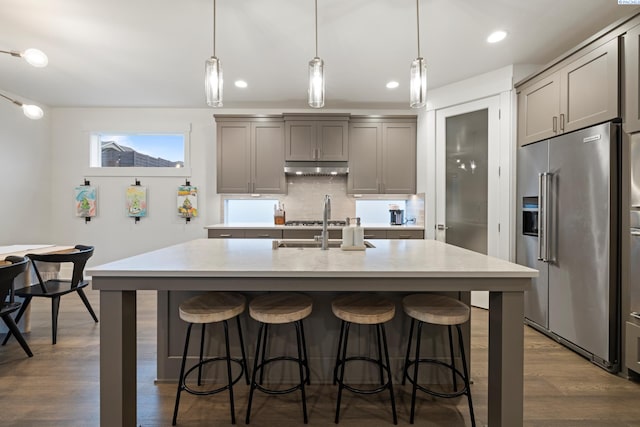 kitchen featuring decorative light fixtures, gray cabinets, high quality fridge, and a center island with sink