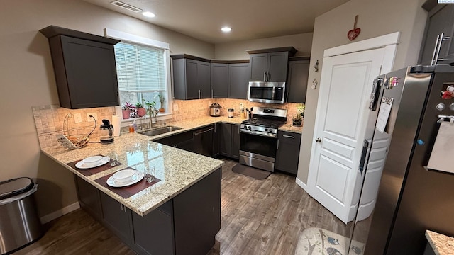 kitchen featuring sink, appliances with stainless steel finishes, kitchen peninsula, hardwood / wood-style flooring, and light stone countertops