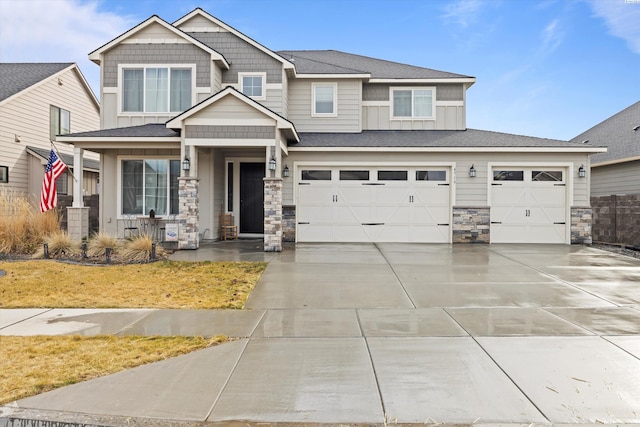 craftsman-style home featuring roof with shingles, board and batten siding, a garage, stone siding, and driveway