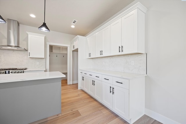 kitchen with hanging light fixtures, wall chimney range hood, white cabinets, and light hardwood / wood-style flooring