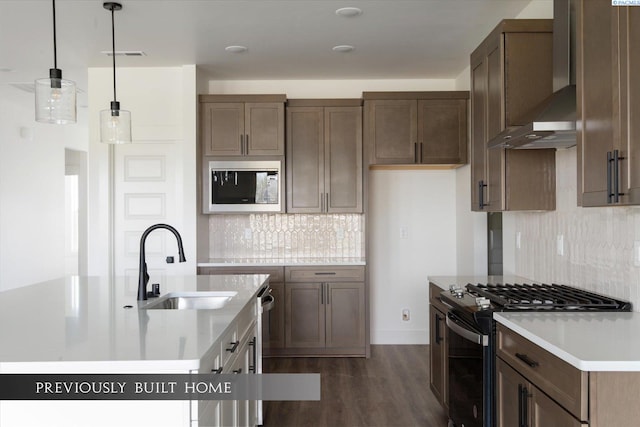 kitchen with pendant lighting, range with gas stovetop, built in microwave, sink, and wall chimney range hood