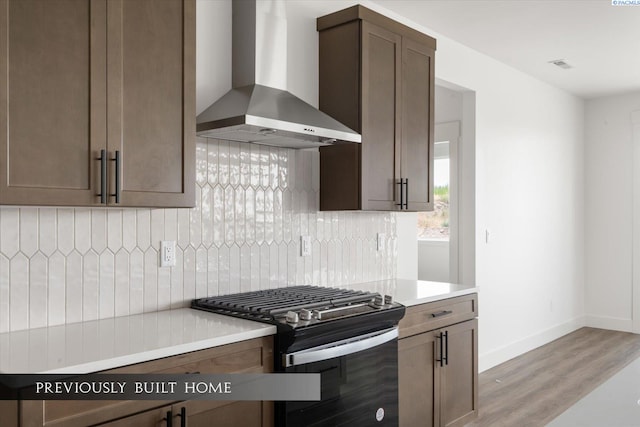 kitchen with tasteful backsplash, wall chimney range hood, gas range oven, and light hardwood / wood-style flooring