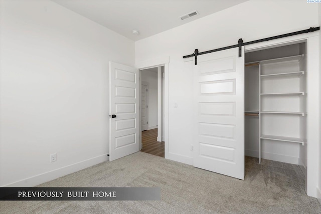 unfurnished bedroom featuring a closet, a barn door, and carpet