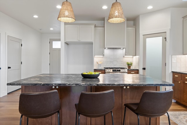 kitchen featuring stainless steel stove, white cabinetry, a kitchen island, decorative light fixtures, and light wood-type flooring