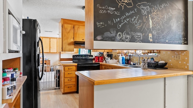 2113 Rainier Ave, Richland, WA 99354 - kitchen featuring black appliances, a sink, under cabinet range hood, a textured ceiling, and light wood finished floors