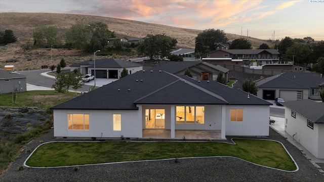 back house at dusk featuring a yard and a patio