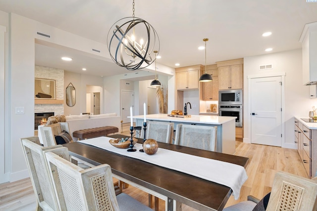 dining area with a stone fireplace, a chandelier, sink, and light wood-type flooring