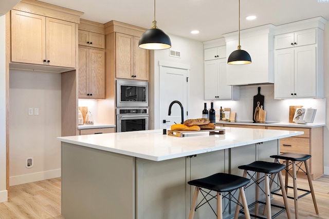 kitchen featuring stainless steel appliances, a kitchen island with sink, pendant lighting, and light wood-type flooring