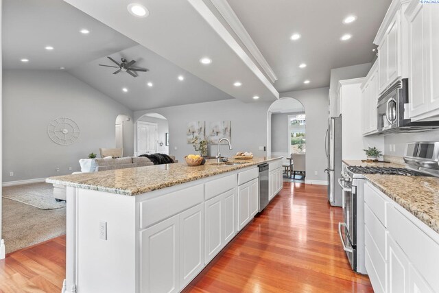 kitchen with open floor plan, arched walkways, appliances with stainless steel finishes, and an island with sink