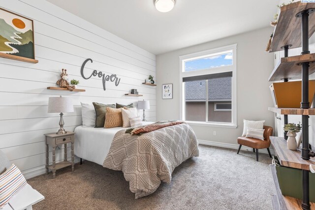 bedroom featuring baseboards, wood walls, and light carpet