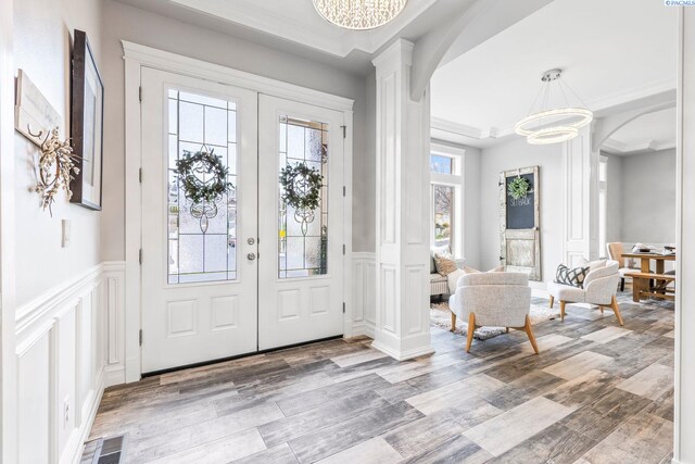 entrance foyer featuring a chandelier, wood finished floors, a decorative wall, arched walkways, and ornate columns