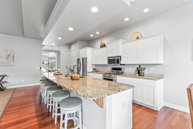kitchen with a kitchen island with sink, stainless steel appliances, a breakfast bar area, and wood finished floors
