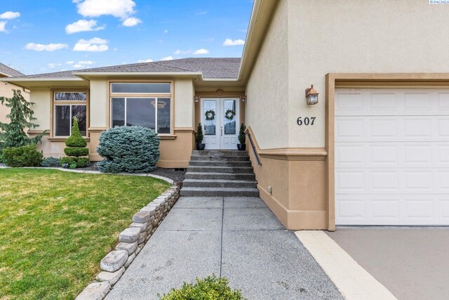 entrance to property with french doors, roof with shingles, stucco siding, a garage, and a yard