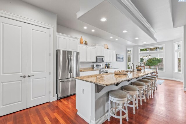 kitchen featuring dark wood-style flooring, stainless steel appliances, white cabinetry, a sink, and a kitchen breakfast bar