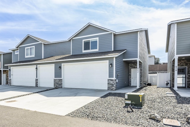 view of front of home featuring an attached garage, roof with shingles, driveway, and stone siding