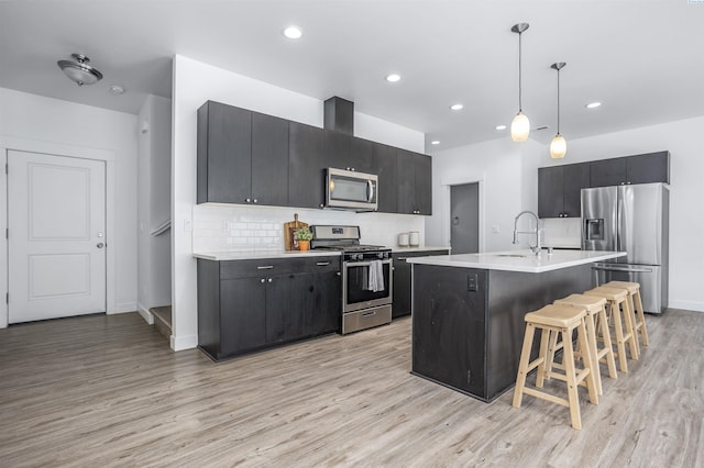 kitchen with light countertops, dark cabinetry, light wood-style floors, stainless steel appliances, and a breakfast bar area