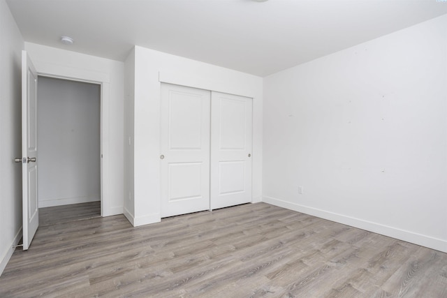 unfurnished bedroom with light wood-type flooring, a closet, and baseboards