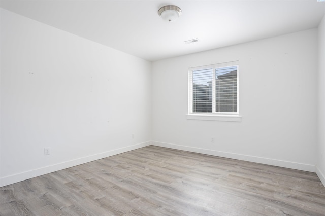 empty room featuring wood finished floors, baseboards, and visible vents
