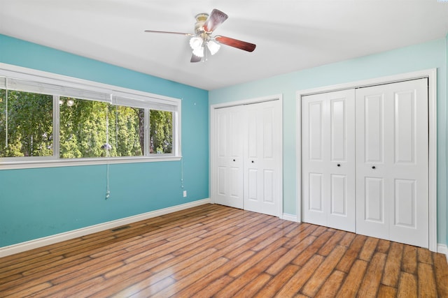 unfurnished bedroom featuring multiple closets, hardwood / wood-style floors, and ceiling fan