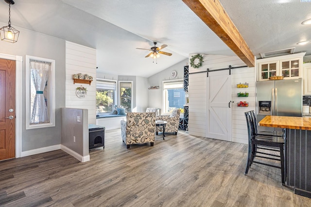 interior space featuring lofted ceiling with beams, a barn door, butcher block counters, wood finished floors, and glass insert cabinets