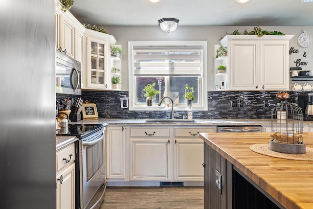 kitchen featuring appliances with stainless steel finishes, butcher block countertops, a sink, and white cabinetry