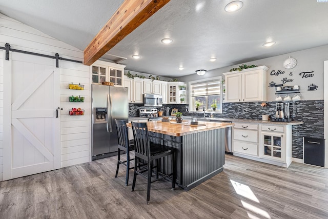 kitchen featuring a barn door, stainless steel appliances, a kitchen island, wood finished floors, and wooden counters