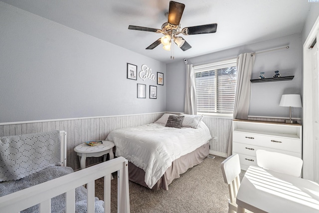 carpeted bedroom featuring a ceiling fan, a wainscoted wall, and wooden walls