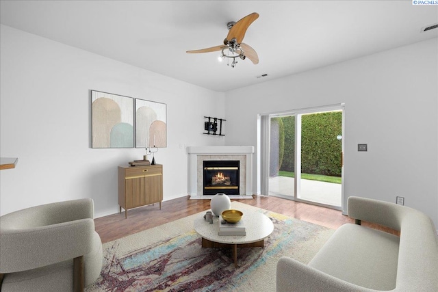 living room featuring a tiled fireplace, wood-type flooring, and ceiling fan