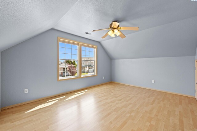 additional living space with visible vents, wood finished floors, lofted ceiling, ceiling fan, and a textured ceiling