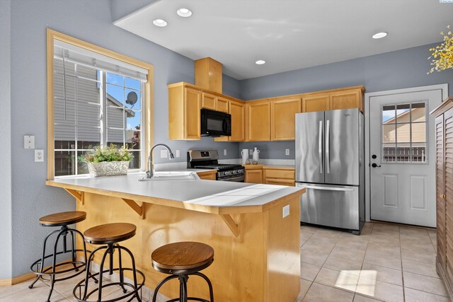 kitchen with a sink, light tile patterned floors, light brown cabinets, and stainless steel appliances
