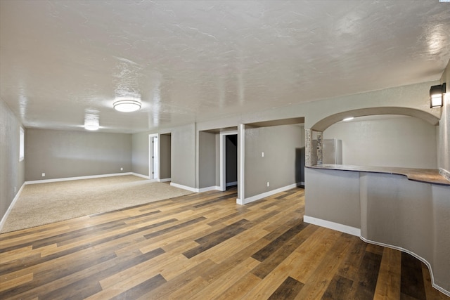 unfurnished room featuring baseboards, arched walkways, a textured ceiling, and wood finished floors